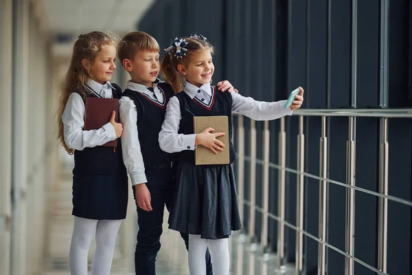 School kids in uniform together with phone and making selfie in corridor. Conception of education.