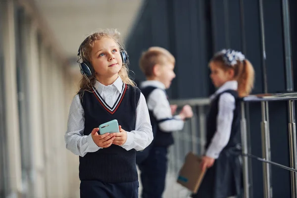 친구들 앞에서 제복을 복도에 있는걸보면 휴대폰 헤드폰을 소녀가 있습니다 교육의 — 스톡 사진