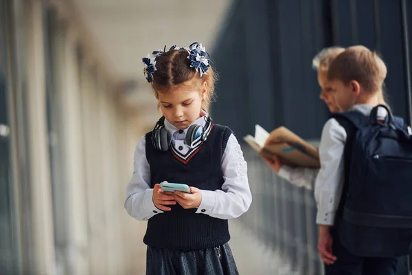 Okul Üniformalı Çocukların Önünde Koridorda Telefon Başında Duran Küçük Kız — Stok fotoğraf