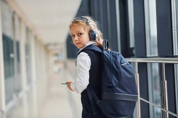 Cute Little School Girl Uniform Headphones Phone Indoors — стоковое фото