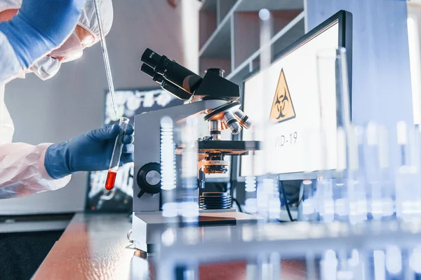 Beyaz koruyucu üniformalı bilim adamları laboratuarda koronavirüs ve kan tüpleriyle çalışıyorlar..