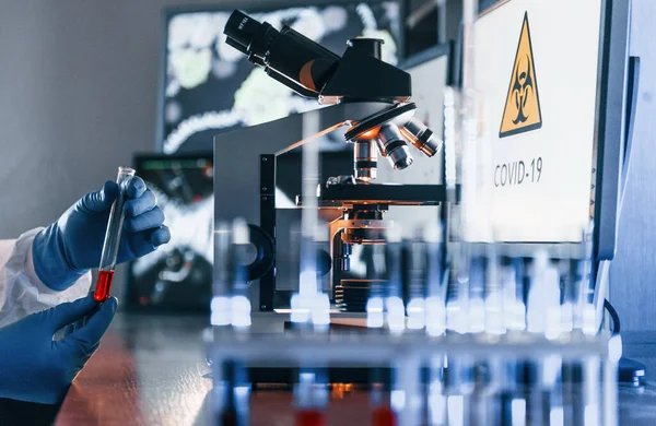 Beyaz koruyucu üniformalı bilim adamları laboratuarda koronavirüs ve kan tüpleriyle çalışıyorlar..