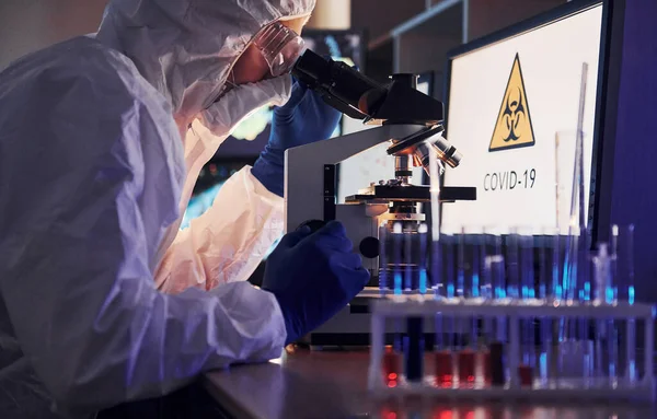 Masadaki bilgili monitörler. Beyaz koruyucu üniformalı bilim adamları laboratuarda koronavirüs ve kan tüpleriyle çalışıyorlar..