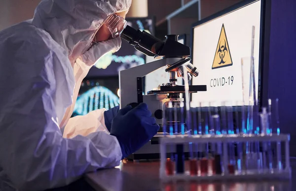 Masadaki bilgili monitörler. Beyaz koruyucu üniformalı bilim adamları laboratuarda koronavirüs ve kan tüpleriyle çalışıyorlar..