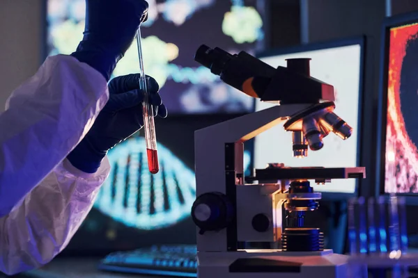 Masadaki bilgili monitörler. Beyaz koruyucu üniformalı bilim adamları laboratuarda koronavirüs ve kan tüpleriyle çalışıyorlar..