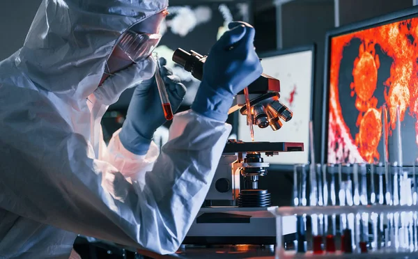 Beyaz koruyucu üniforma giyen bilim adamları verilerle birlikte laboratuvarda koronavirüs ve kan tüpleriyle çalışıyorlar..