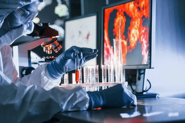 Beyaz koruyucu üniformalı bilim adamları laboratuarda koronavirüs ve kan tüpleriyle çalışıyorlar..