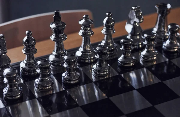 Üzerinde metal figürler olan satranç tahtası gündüz vakti masanın üstünde..