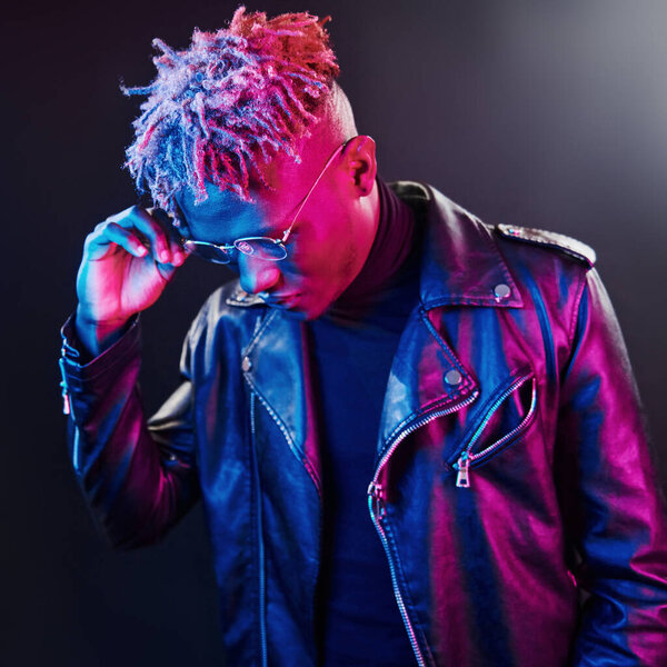 Futuristic neon lighting. Young african american man in glasses standing in studio.