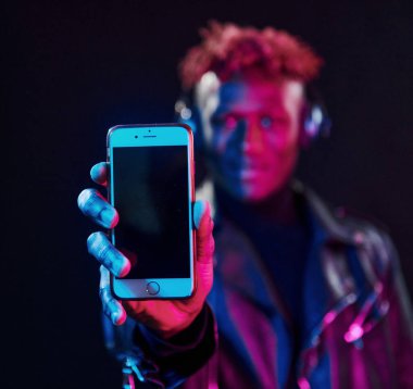 Telefon ve kulaklıkla. Fütürist neon ışıkları. Stüdyodaki Afrikalı Amerikalı genç adam..