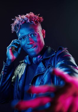 Şık gözlükler ve kablosuz kulaklıklar. Fütürist neon ışıkları. Stüdyodaki Afrikalı Amerikalı genç adam..