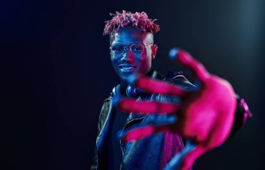 Şık gözlükler ve kablosuz kulaklıklar. Fütürist neon ışıkları. Stüdyodaki Afrikalı Amerikalı genç adam..