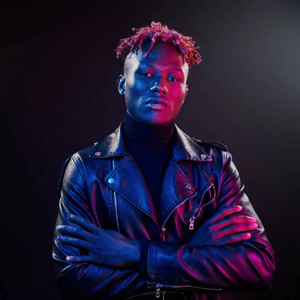 Fütürist neon ışıkları. Stüdyoda kollarını kavuşturmuş genç Afrikalı Amerikalı adam..