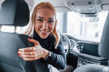 Rear view of beautiful blonde in elegant clothes that sitting inside of modern car.