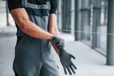 Gri üniformalı bir adam eldiven giyiyor ve modern büyük ofiste çalışmaya hazırlanıyor..