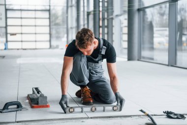 Gri üniformalı adam gündüz vakti modern büyük ofiste kapalı alanda çalışıyor..