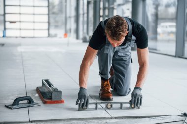 Gri üniformalı adam gündüz vakti modern büyük ofiste kapalı alanda çalışıyor..