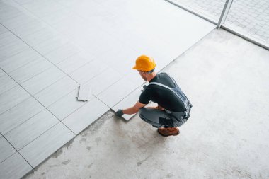 Top view of man in grey uniform that installing plate indoors in modern big office at daytime.