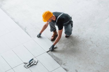 Installation of plate. Man in grey uniform and orange hard hat works indoors in modern big office at daytime.