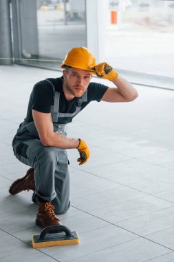 Gündüz vakti modern büyük ofiste gri üniformalı bir adam kameraya poz veriyor..