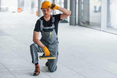 Gündüz vakti modern büyük ofiste gri üniformalı bir adam kameraya poz veriyor..