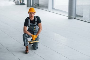 Gündüz vakti modern büyük ofiste gri üniformalı bir adam kameraya poz veriyor..