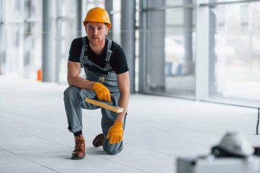 Gündüz vakti modern büyük ofiste gri üniformalı bir adam kameraya poz veriyor..