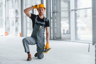 Gündüz vakti modern büyük ofiste gri üniformalı bir adam kameraya poz veriyor..