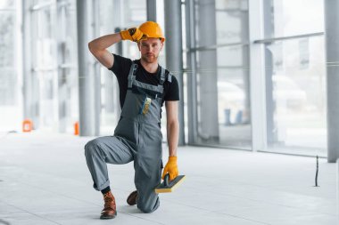 Gündüz vakti modern büyük ofiste gri üniformalı bir adam kameraya poz veriyor..