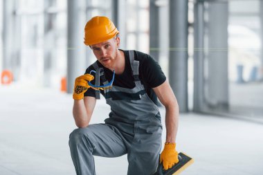 Gündüz vakti modern büyük ofiste gri üniformalı bir adam kameraya poz veriyor..