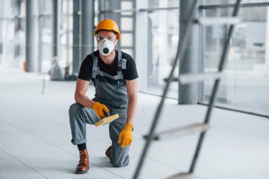 Gündüz vakti modern büyük ofiste gri üniformalı bir adam kameraya poz veriyor..