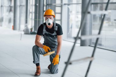 Gündüz vakti modern büyük ofiste gri üniformalı bir adam kameraya poz veriyor..