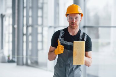 Gri üniformalı bir adamın portresi. Gündüz vakti modern bir ofiste elinde ekipmanla ayakta duruyor..