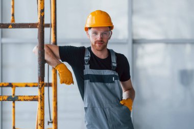 İnşaatın yanındaki gri üniformalı adam modern büyük ofiste gündüz vakti kapalı bir yerde mola veriyor..