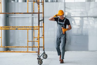 İnşaatın yanındaki gri üniformalı adam modern büyük ofiste gündüz vakti kapalı bir yerde mola veriyor..