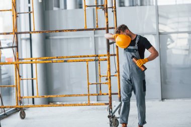 İnşaatın yanındaki gri üniformalı adam modern büyük ofiste gündüz vakti kapalı bir yerde mola veriyor..