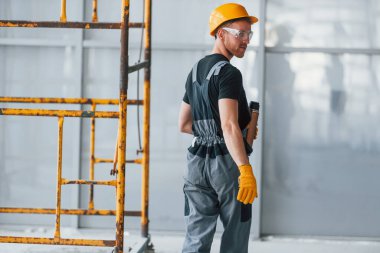 İnşaatın yanındaki gri üniformalı adam modern büyük ofiste gündüz vakti kapalı bir yerde mola veriyor..