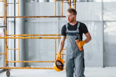 İnşaatın yanındaki gri üniformalı adam modern büyük ofiste gündüz vakti kapalı bir yerde mola veriyor..