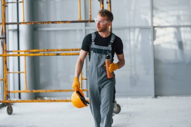 İnşaatın yanındaki gri üniformalı adam modern büyük ofiste gündüz vakti kapalı bir yerde mola veriyor..