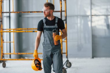 İnşaatın yanındaki gri üniformalı adam modern büyük ofiste gündüz vakti kapalı bir yerde mola veriyor..