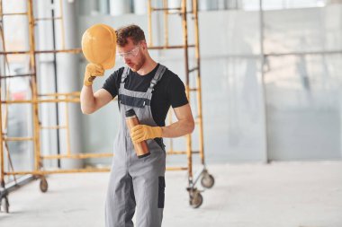 İnşaatın yanındaki gri üniformalı adam modern büyük ofiste gündüz vakti kapalı bir yerde mola veriyor..