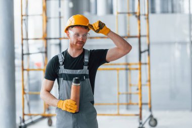 İnşaatın yanındaki gri üniformalı adam modern büyük ofiste gündüz vakti kapalı bir yerde mola veriyor..