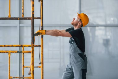 Gri üniformalı adam gündüz vakti modern büyük ofiste kapalı alanda inşaat işinde çalışıyor..