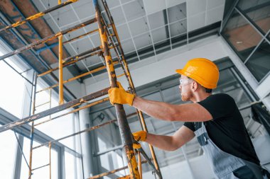 Gri üniformalı adam gündüz vakti modern büyük ofiste kapalı alanda inşaat işinde çalışıyor..