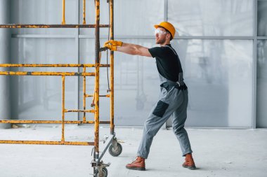 Gri üniformalı adam gündüz vakti modern büyük ofiste kapalı alanda inşaat işinde çalışıyor..