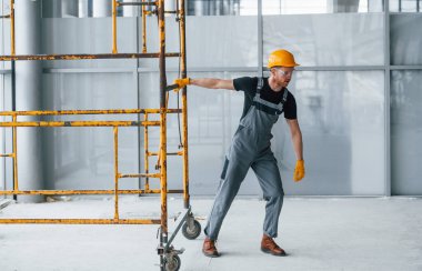 Gri üniformalı adam gündüz vakti modern büyük ofiste kapalı alanda inşaat işinde çalışıyor..