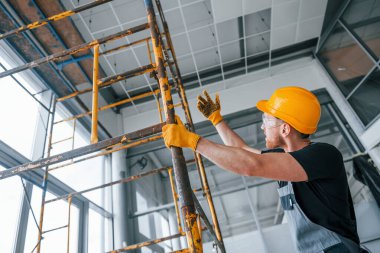 Gri üniformalı adam gündüz vakti modern büyük ofiste kapalı alanda inşaat işinde çalışıyor..