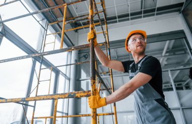 Man in grey uniform works with construction indoors in modern big office at daytime.