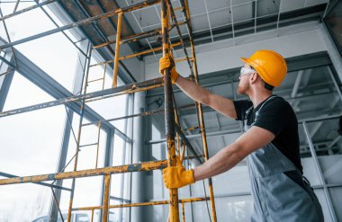 Man in grey uniform works with construction indoors in modern big office at daytime.
