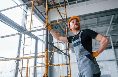 Man in grey uniform works with construction indoors in modern big office at daytime.